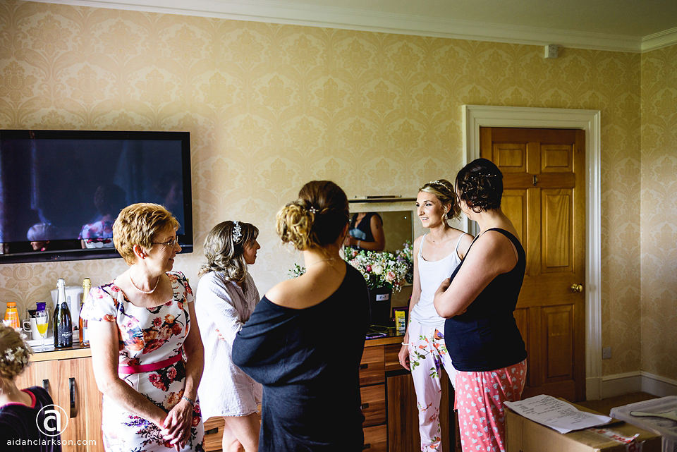 A group of bridesmaids at Kenwick Park, engrossed by a wedding broadcast on the television in a room.