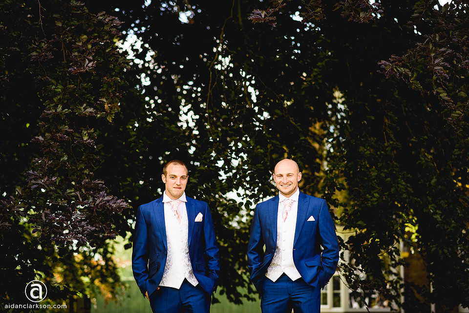 Two grooms standing in front of a tree at their Kenwick Park wedding.