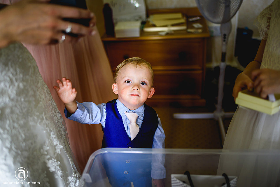 A little boy in a suit and tie is standing in front of a dresser at a wedding.
