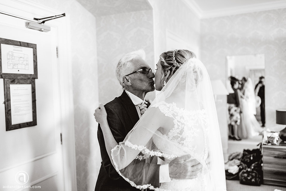 A black and white photo of a bride kissing her father during their wedding at Kenwick Park.