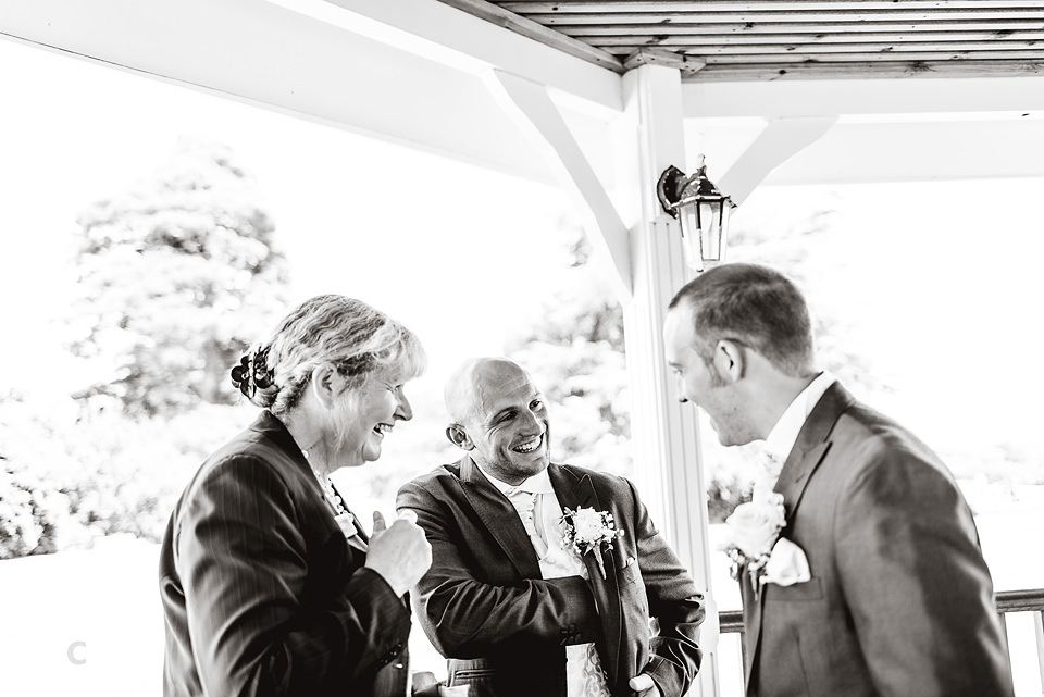 A black and white photo of a wedding groom and groomsmen talking at Kenwick Park.