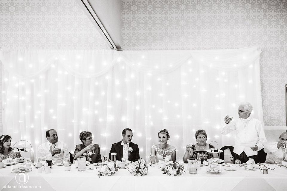 A black and white photo capturing a wedding party at Kenwick Park, gathered around a table.