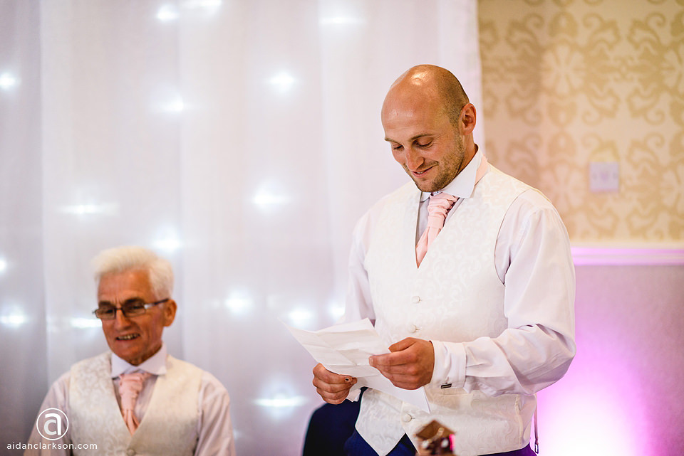 A man is reading a letter at a wedding ceremony in Kenwick Park.