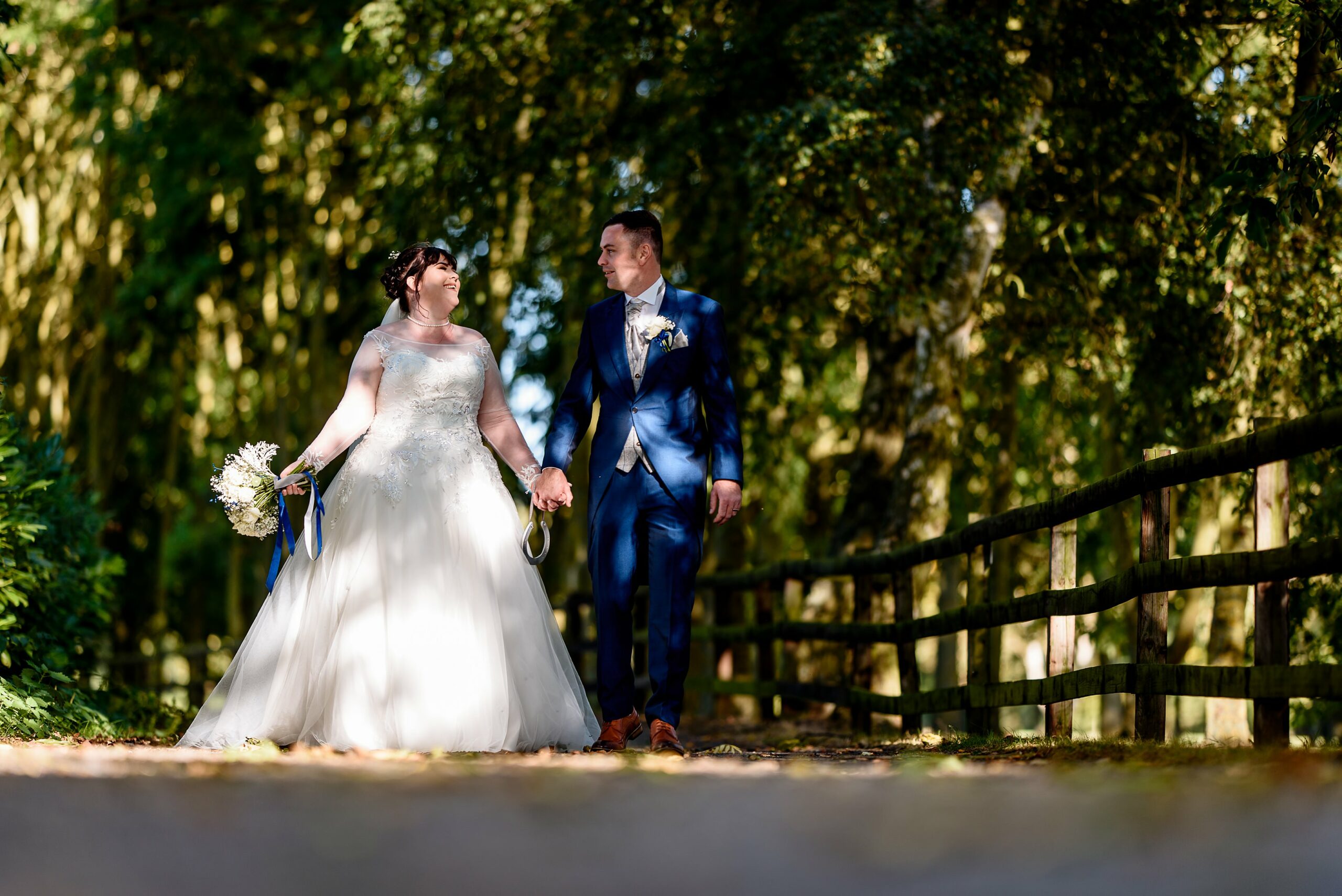 A bride and groom walking down a path in the Laceby Manor woods.