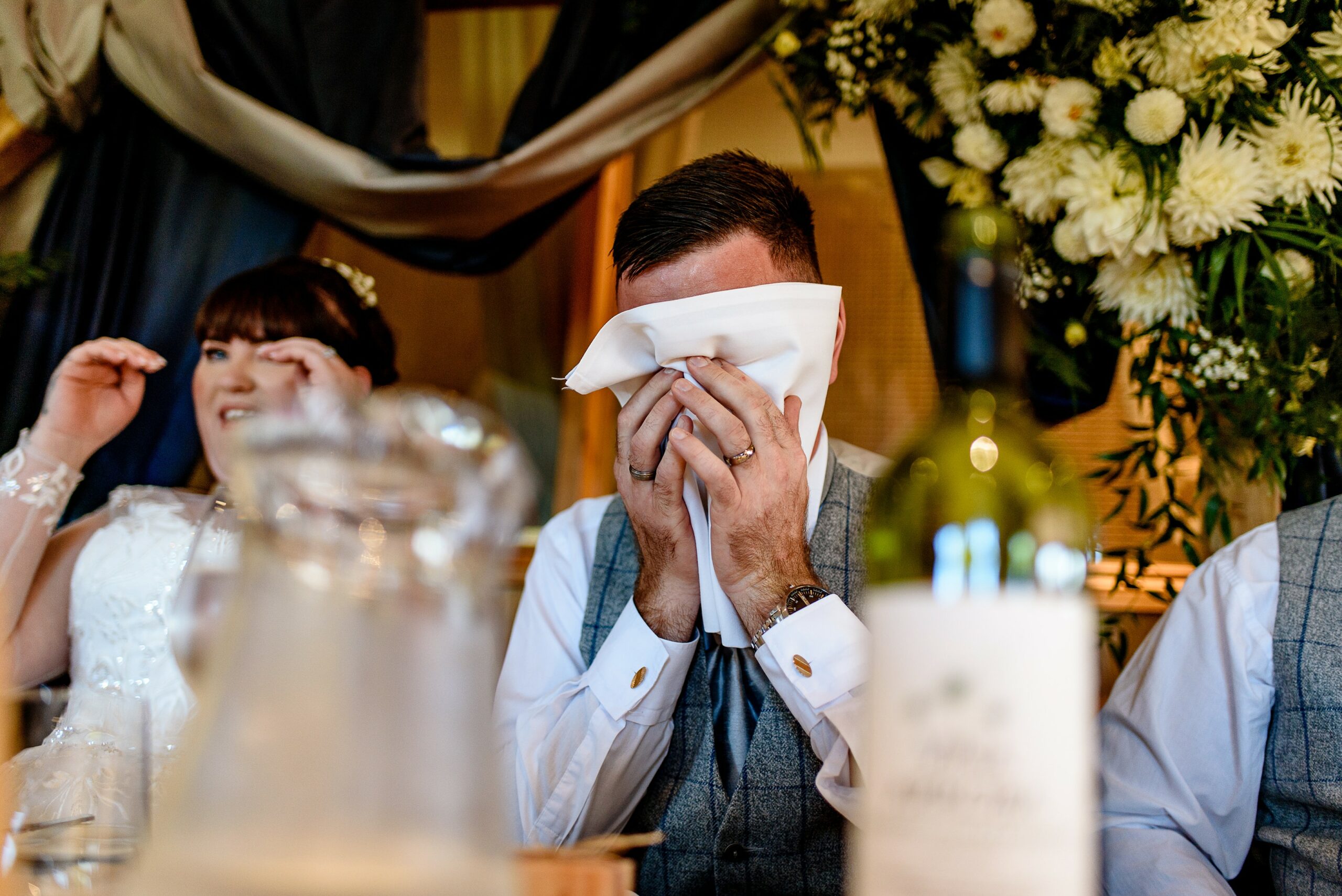 A groom is wiping his eyes with a tissue at Laceby Manor wedding.