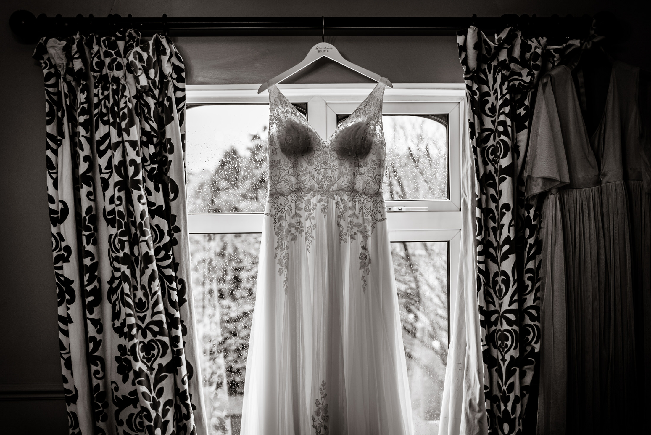 A wedding dress hanging in front of a window at Brackenborough Hotel.