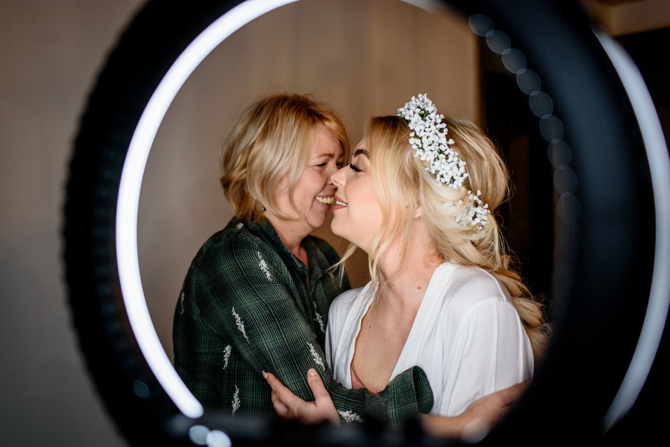 Two women hugging in front of a mirror at a wedding.
