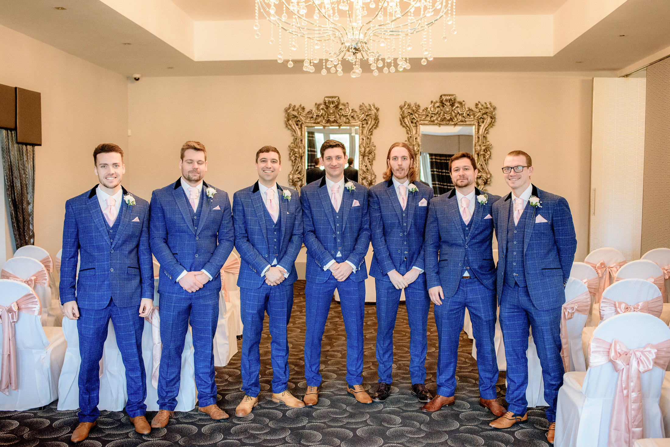 Groomsmen standing in front of a chandelier at a Brackenborough Hotel wedding.