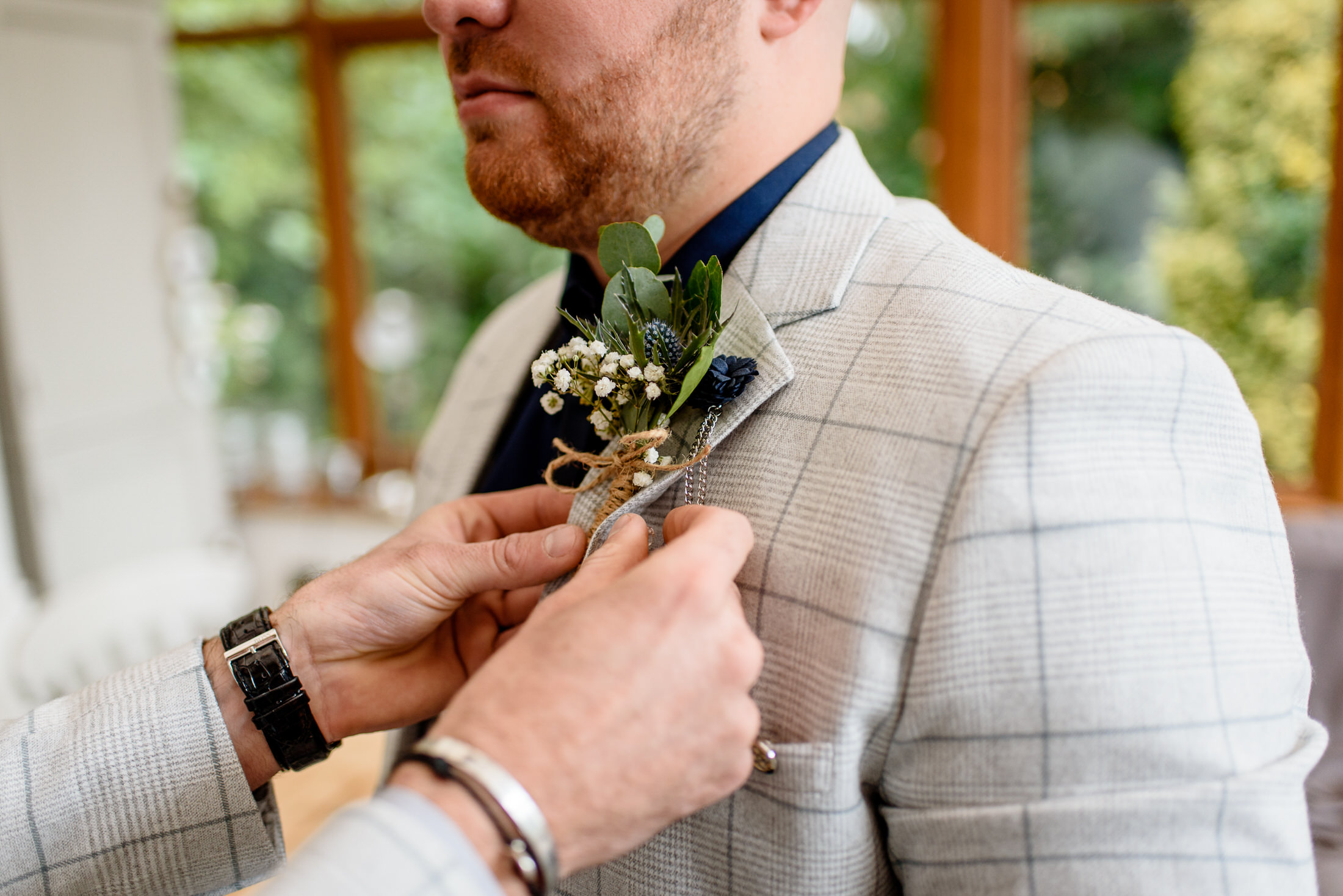 A man in a suit carefully placing a boutonniere in the Scrivelsby Walled Garden for a wedding.