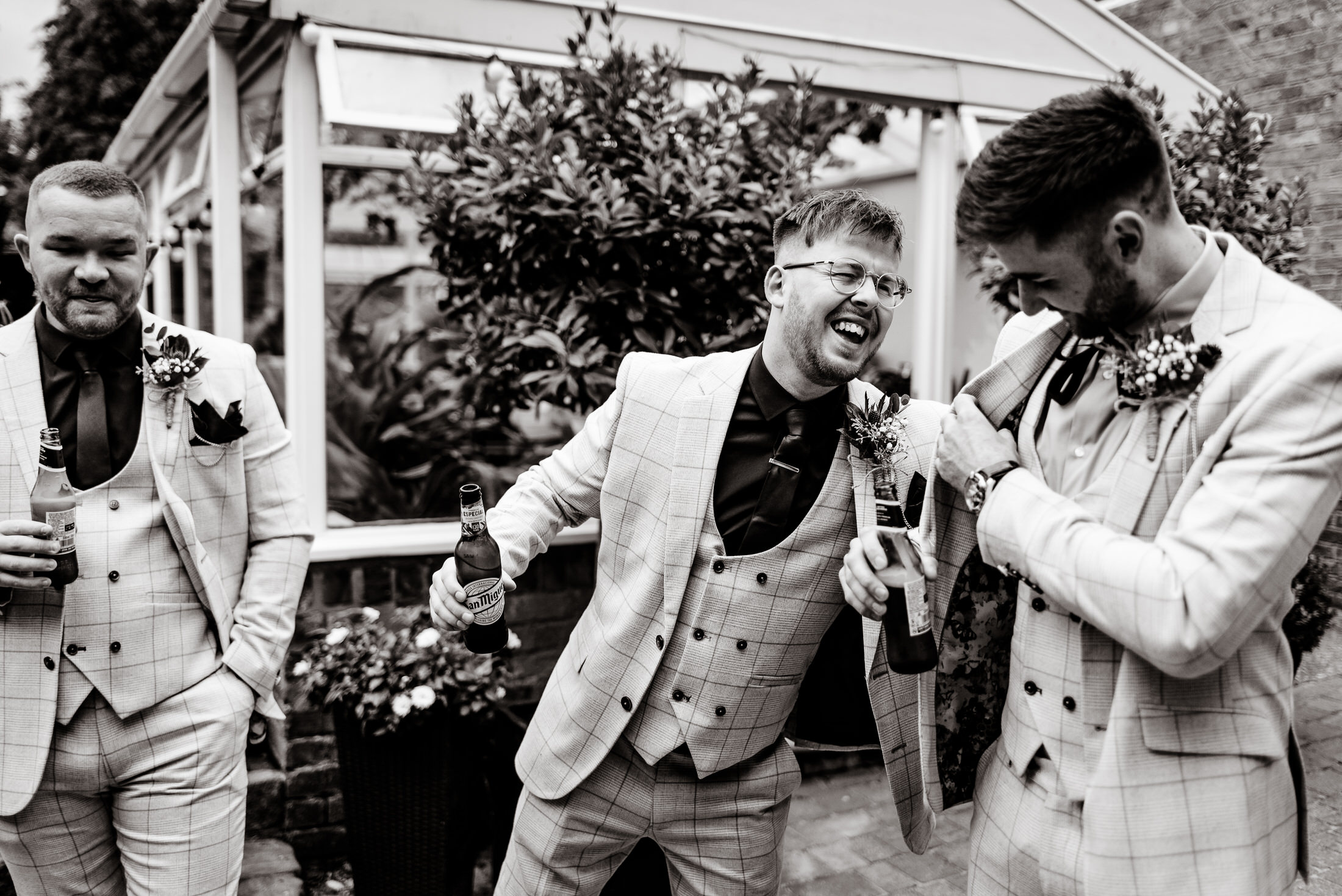 A group of groomsmen laughing in a black and white wedding photo.