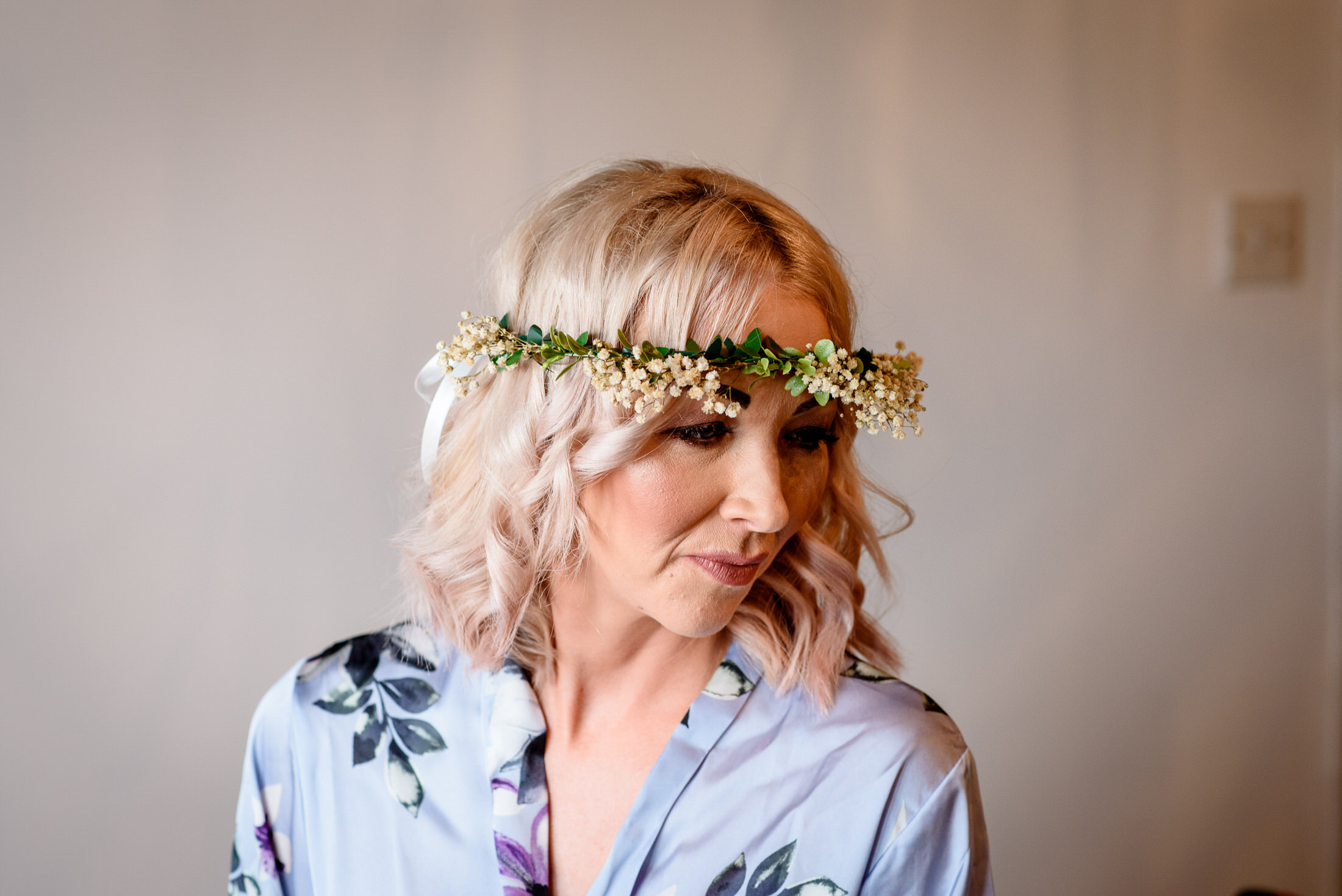 A woman wearing a floral crown at a wedding in front of a mirror.