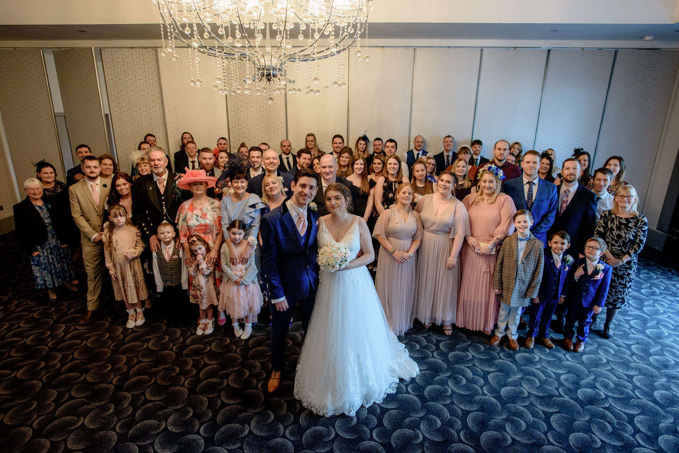 A wedding party posing in front of a chandelier at the Brackenborough Hotel wedding.