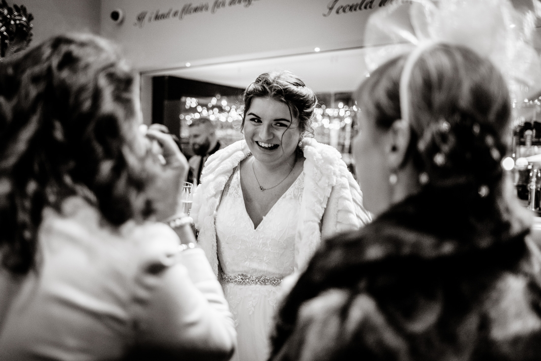 A bride smiles in front of a mirror at her wedding at Brackenborough Hotel.