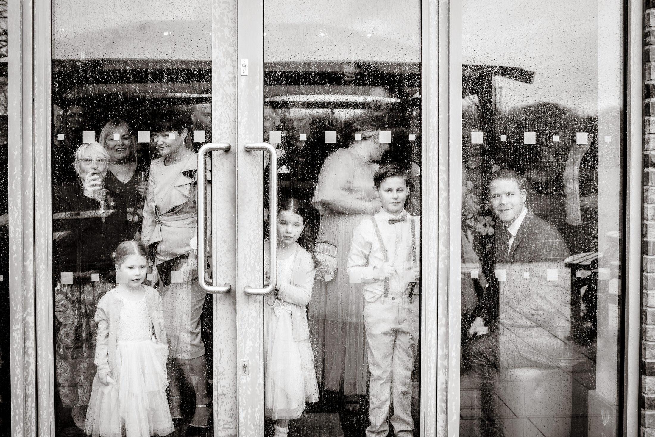 A group of people standing behind glass doors at the Brackenborough Hotel wedding.