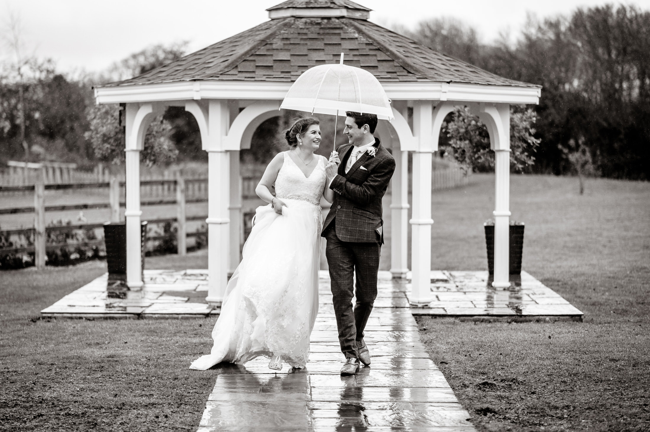 A bride and groom holding an umbrella in front of a gazebo at Brackenborough Hotel on their wedding day.