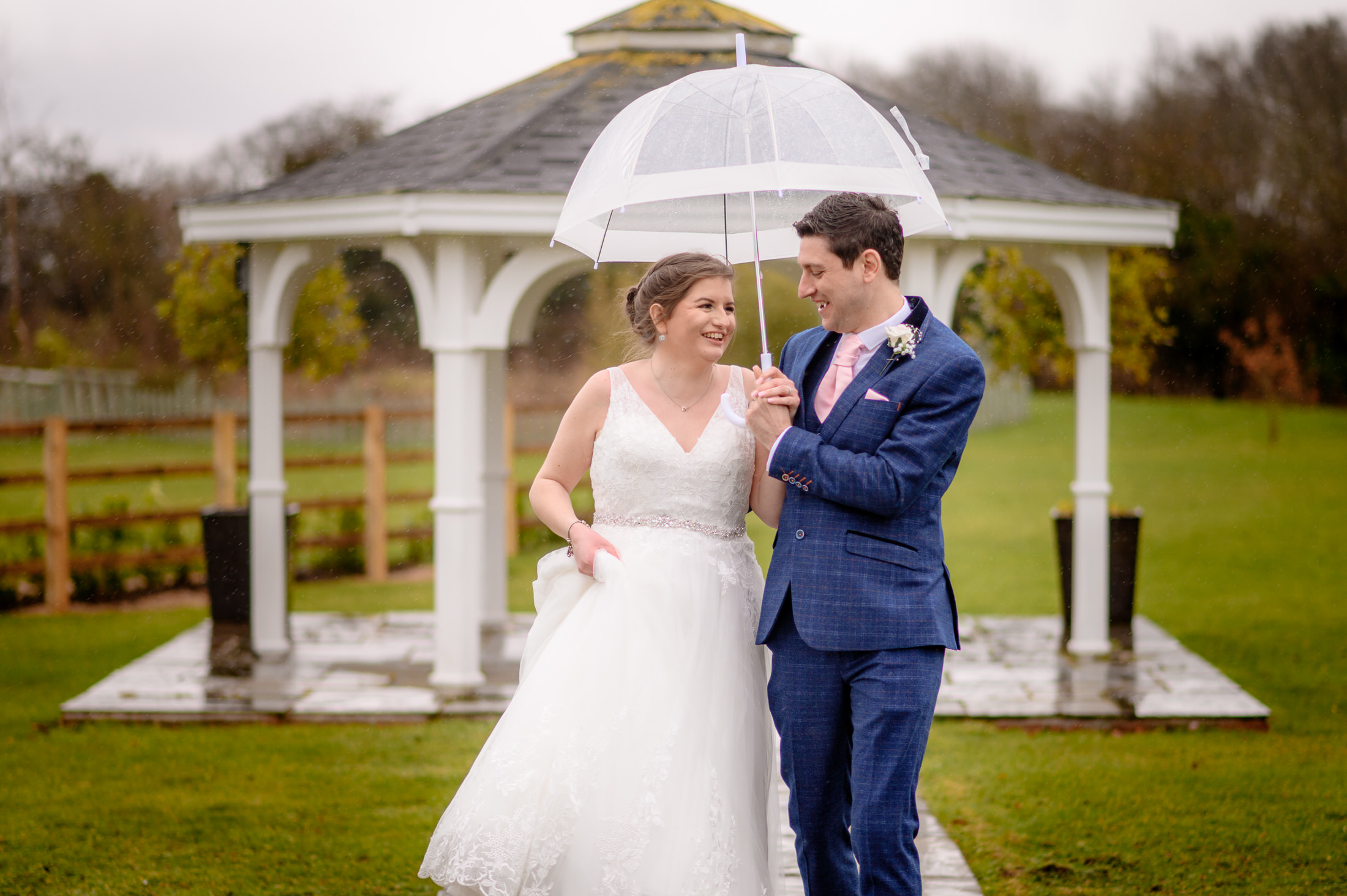 A man and woman holding umbrellas at a beautiful Brackenborough Hotel wedding venue.