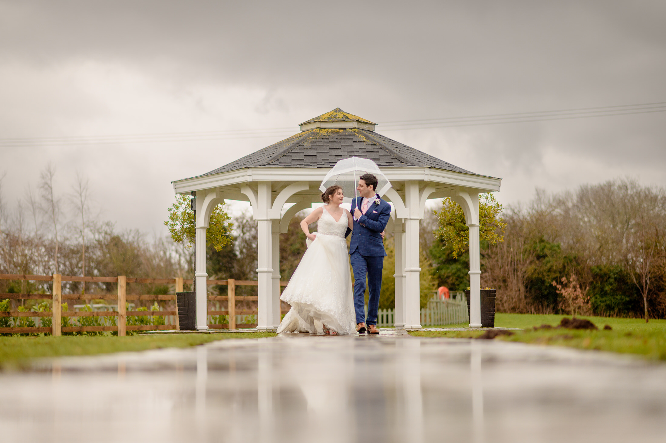A couple in wedding attire, standing under an umbrella at the Brackenborough Hotel wedding.