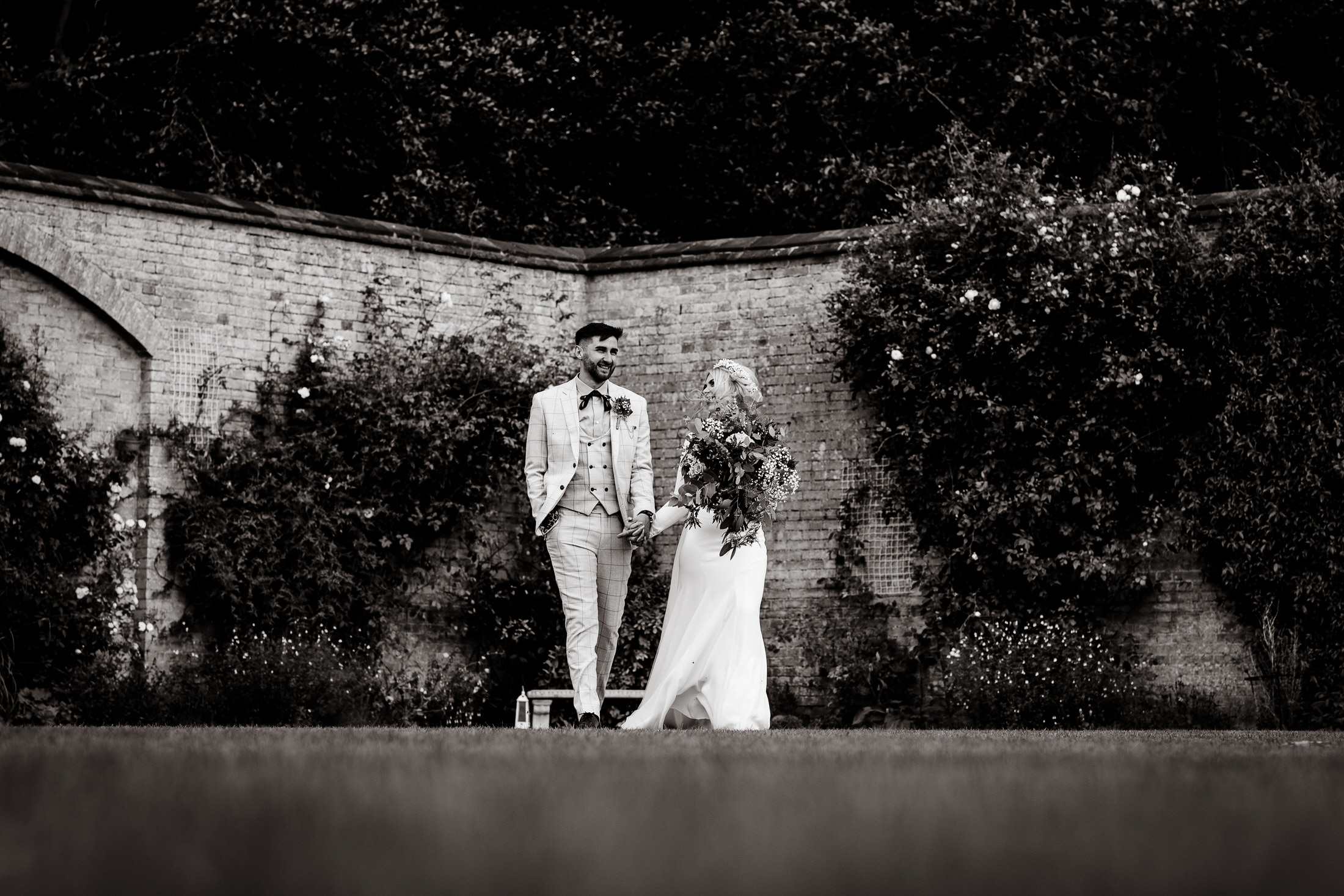 A black and white photo of a bride and groom standing in front of the Scrivelsby Walled Garden.