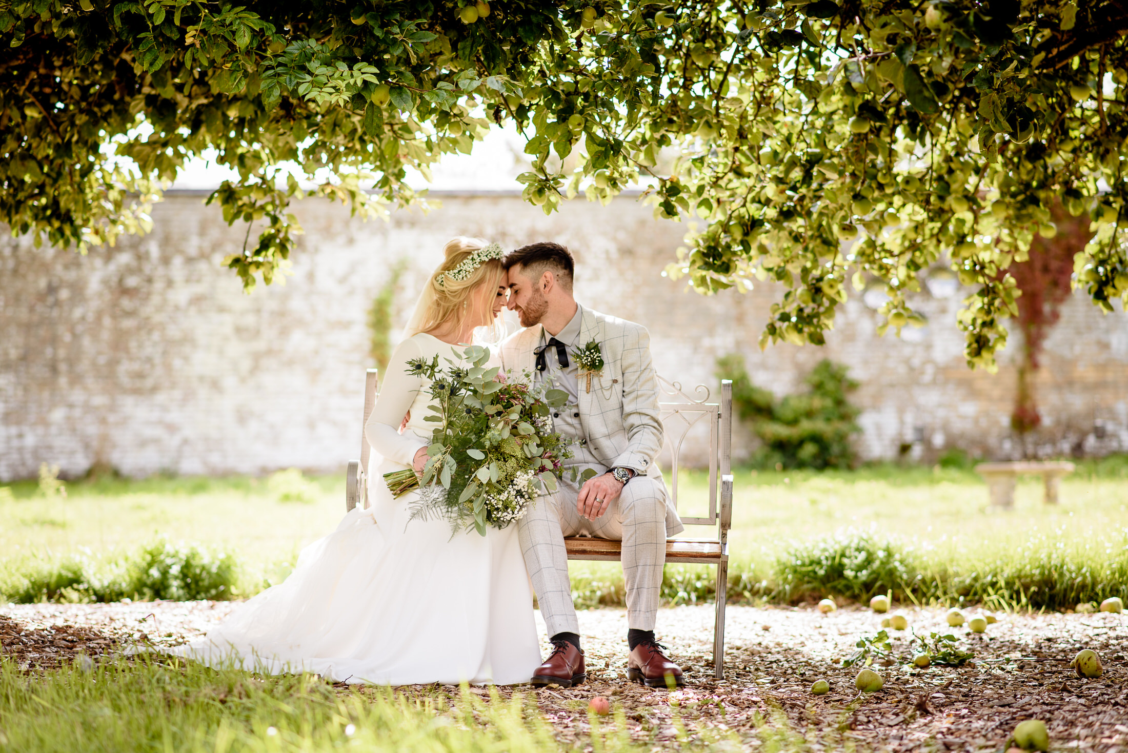 A wedding couple sitting on a bench under an apple tree in the Scrivelsby Walled Garden.