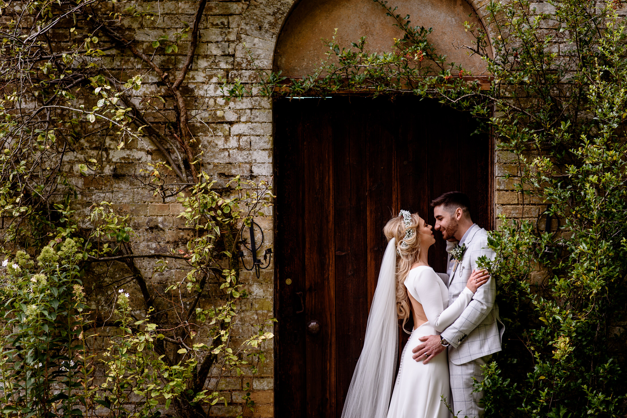 A wedding couple kisses in front of a wooden door at Scrivelsby Walled Garden.