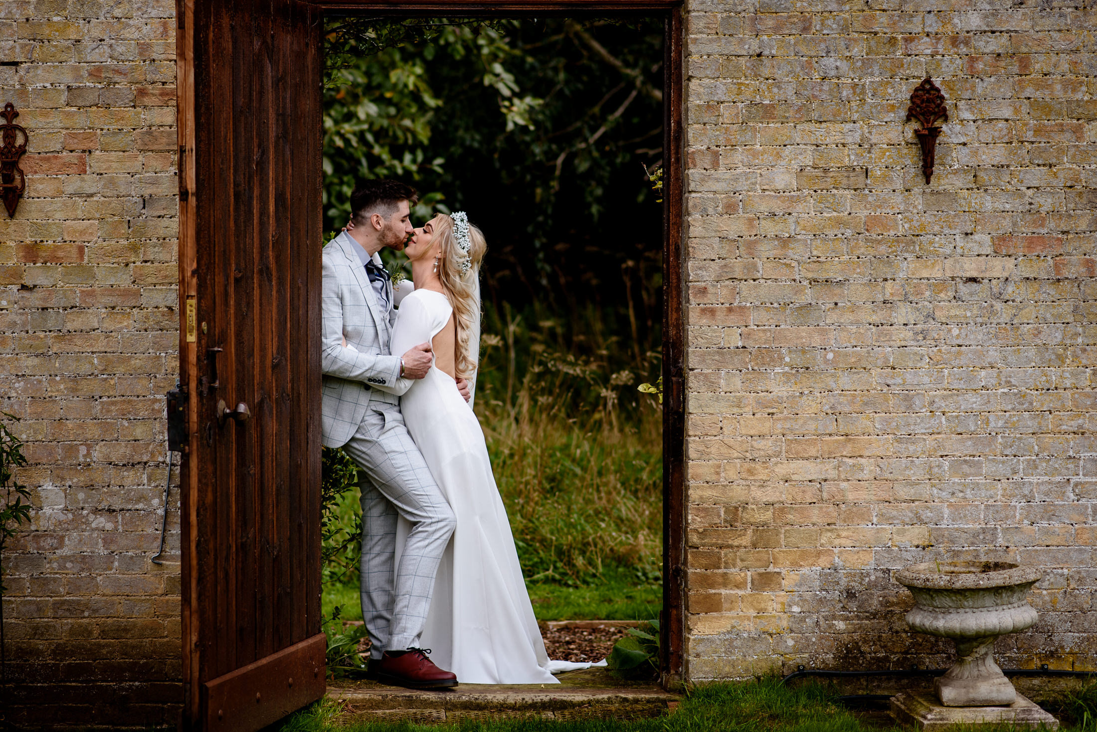 A wedding couple kissing in front of an open door at the Scrivelsby Walled Garden.