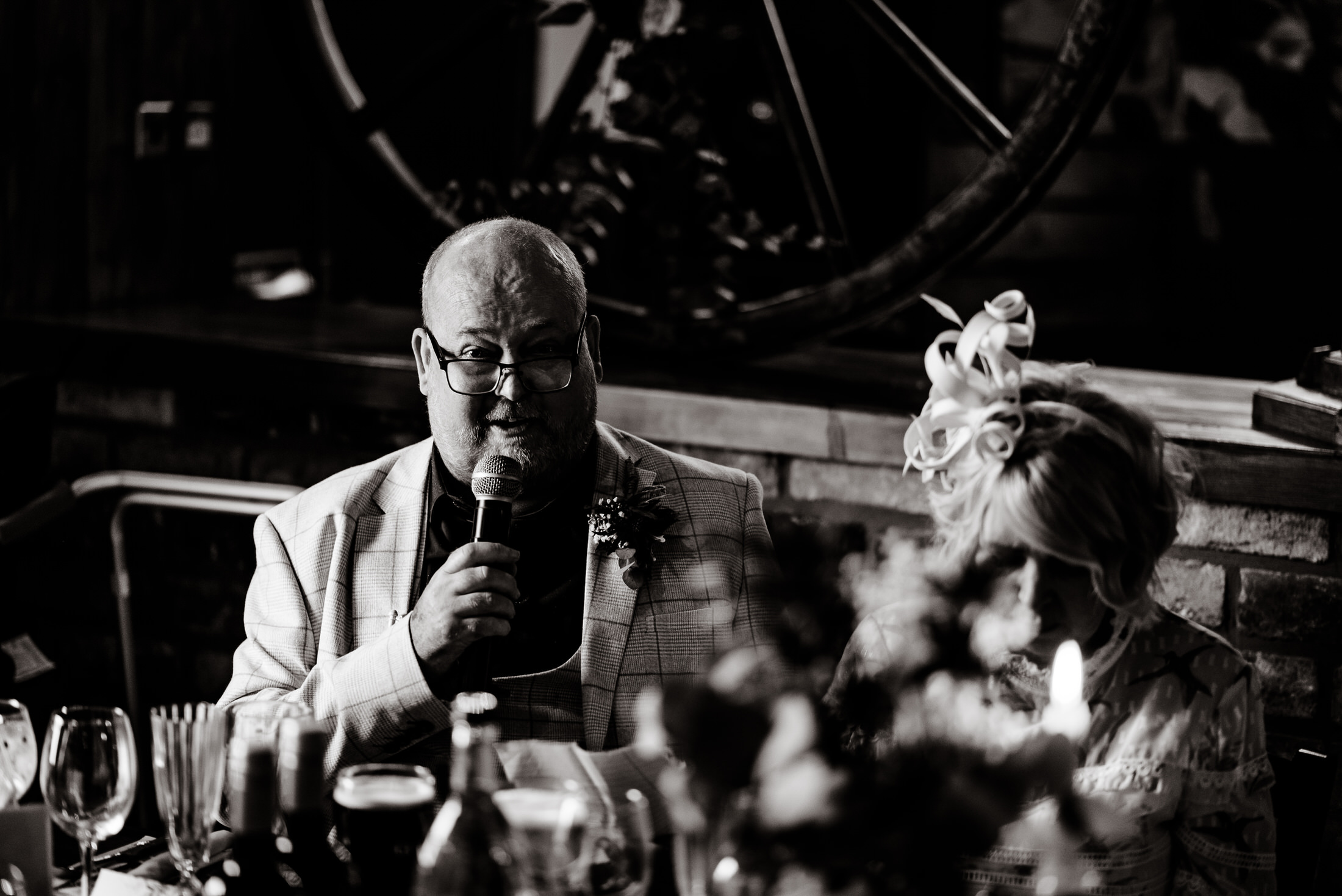 At a wedding reception, a man is passionately speaking into a microphone at a table in the picturesque Scrivelsby Walled Garden.