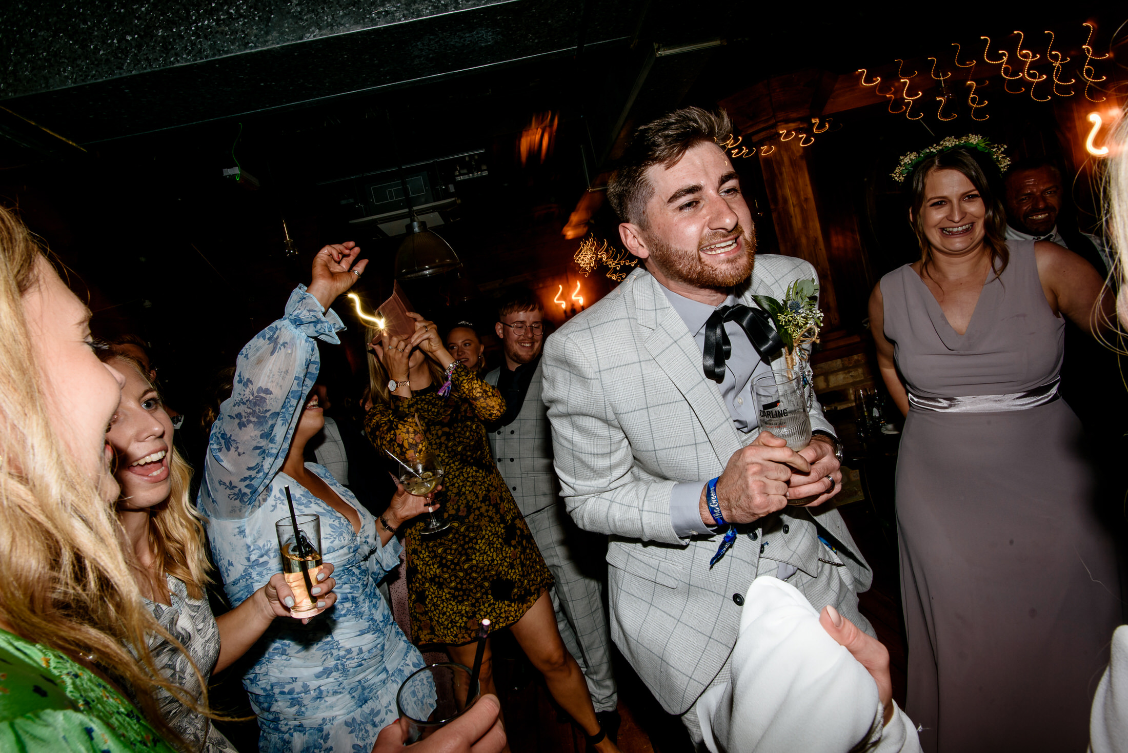 A man in a suit is gracefully holding a glass of wine at a wedding.