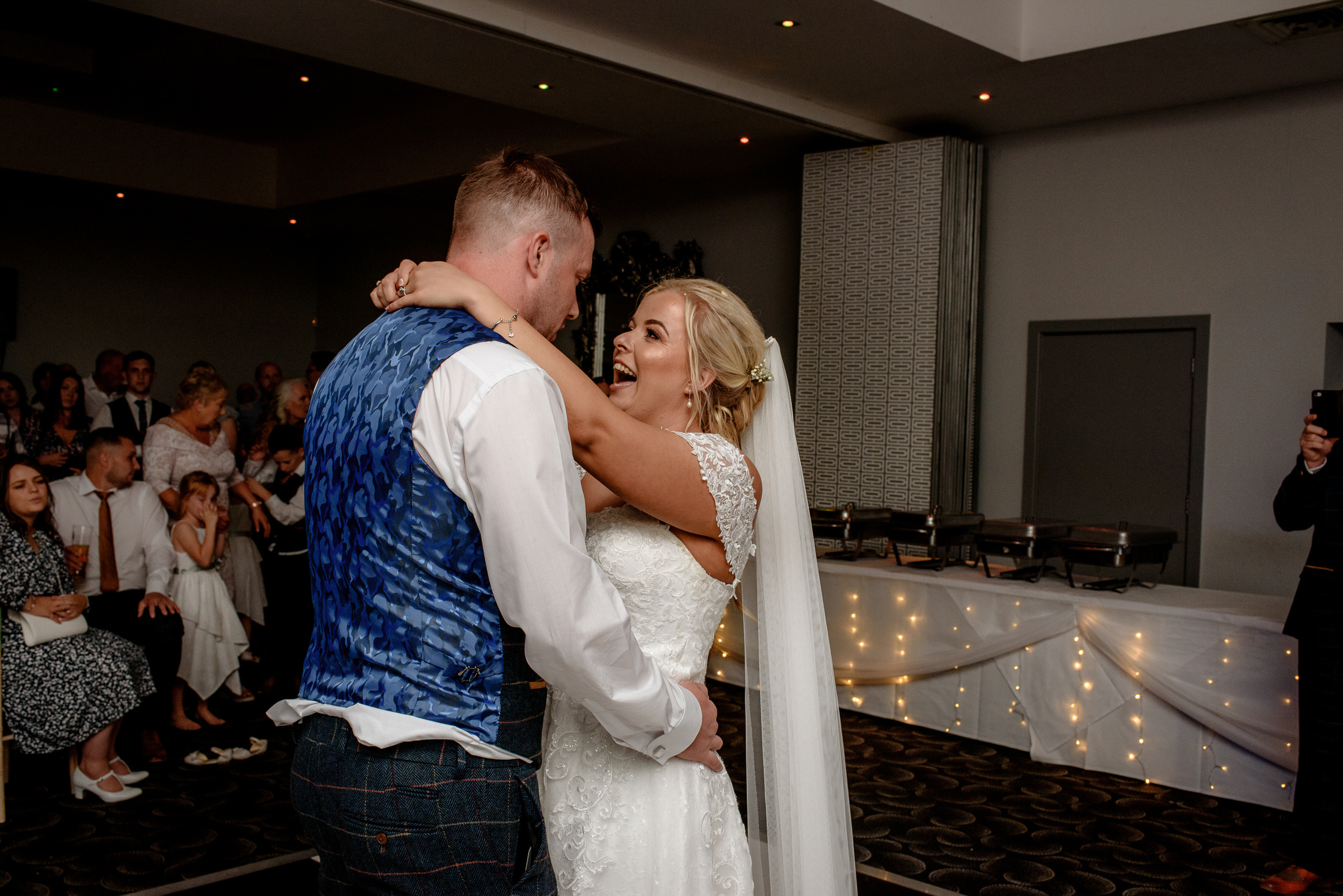 At the Brackenborough Hotel, a bride and groom glide across the dance floor at their wedding reception, surrounded by seated guests.